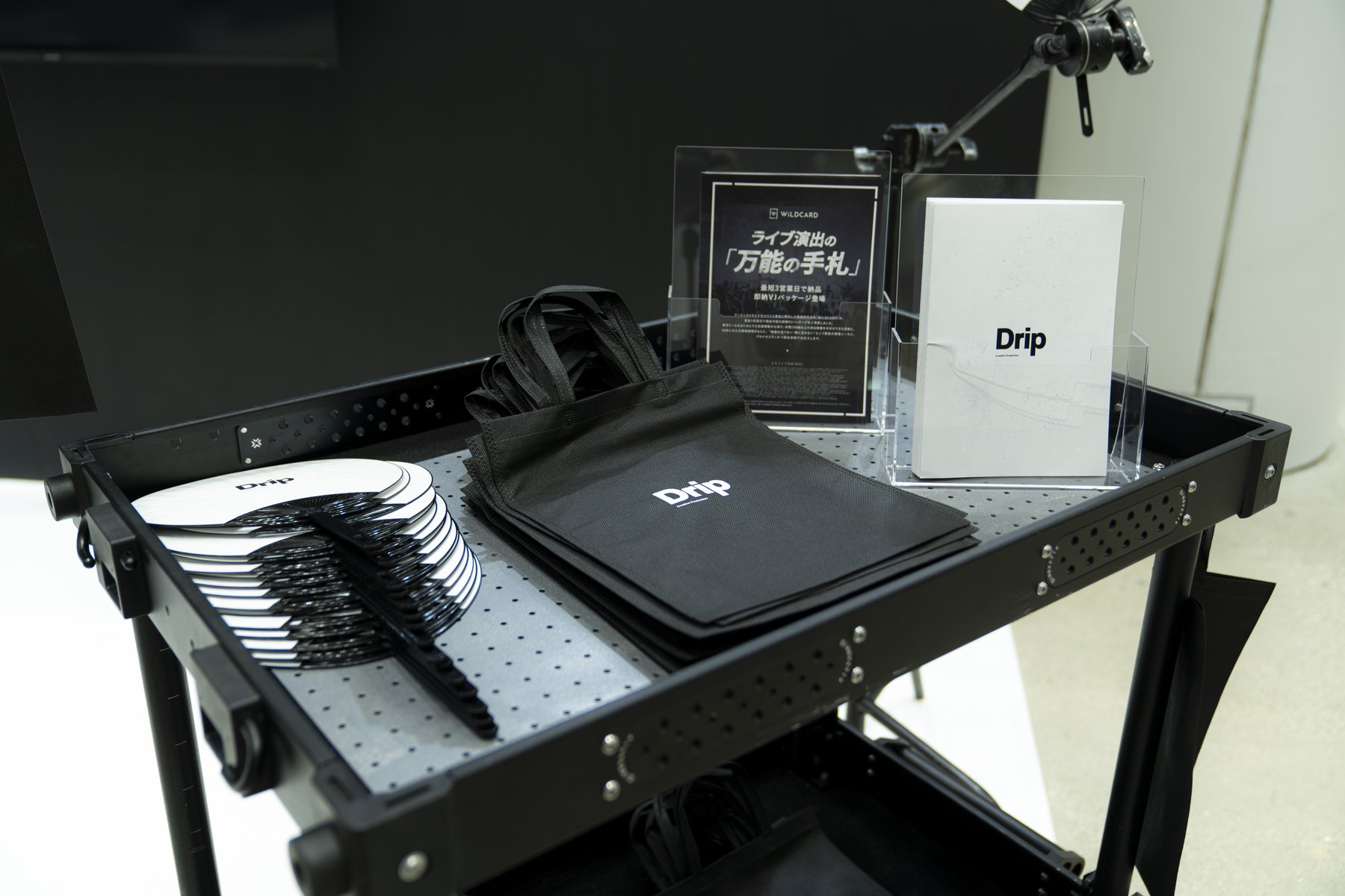 Dripロゴ入りのうちわと黒いトートバッグを並べたノベルティ展示